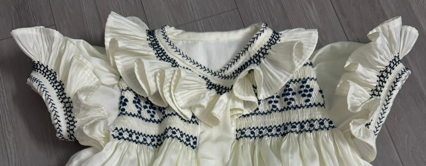 Cream dress with navy smocking on chest sleeve and collar