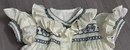 Cream dress with navy smocking on chest sleeve and collar